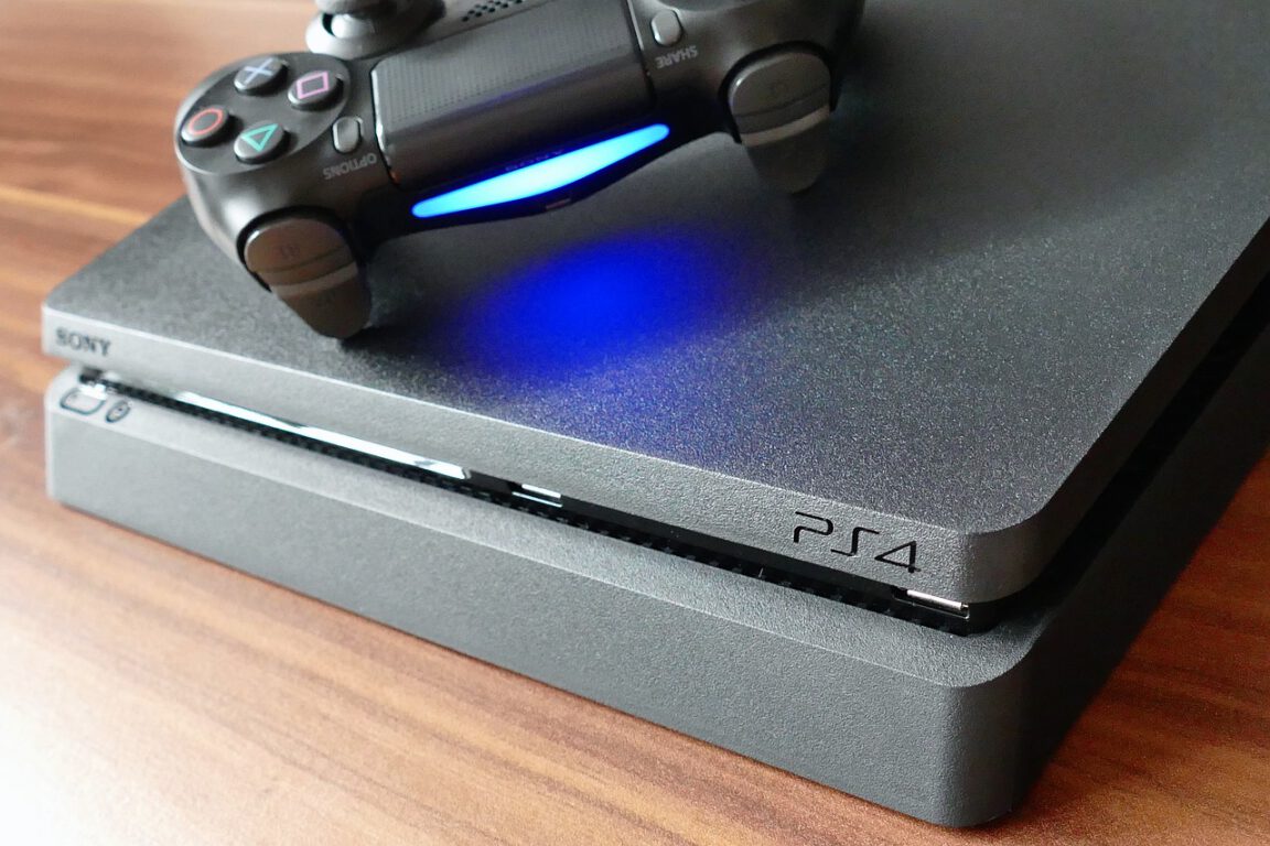 A picture of the PS4 game console with a controller sitting on top of it. 