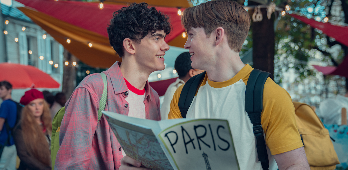 Joe Locke as Charlie and Kit Connor as Nick in a scene from Heartstopper season two. They're gazing at each other over a Paris guidebook.