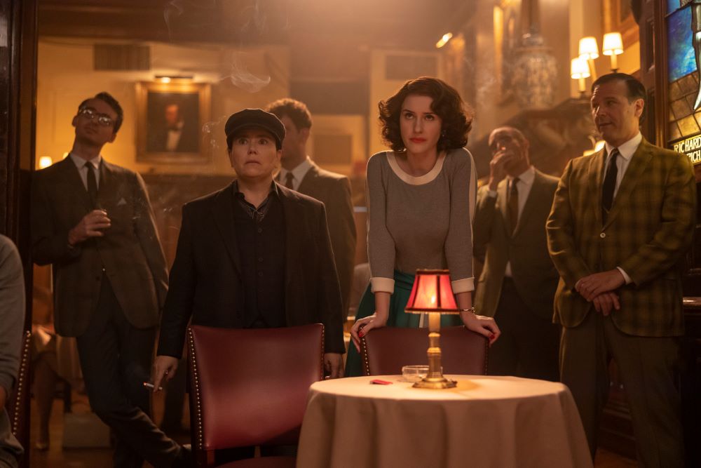 Susie and Midge stand in a packed comedy club while looking at the stage in The Marvelous Mrs. Maisel Season 5 Episode 9, "Four Minutes."