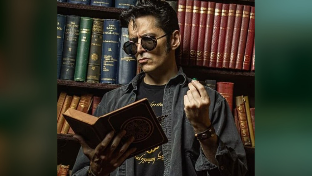 Headshot of Mark Meer reading a book and holding a D20.