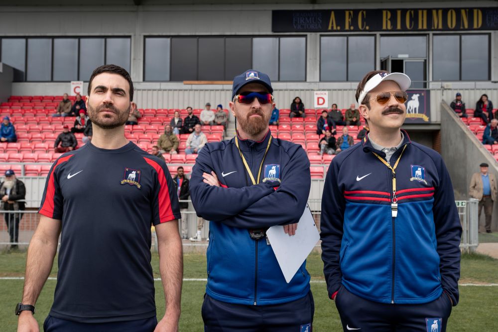 Roy, Coach Beard and Ted stand on the pitch during practice while looking focused in Ted Lasso Season 3 Episode 9, "La Locker Room Aux Folles."