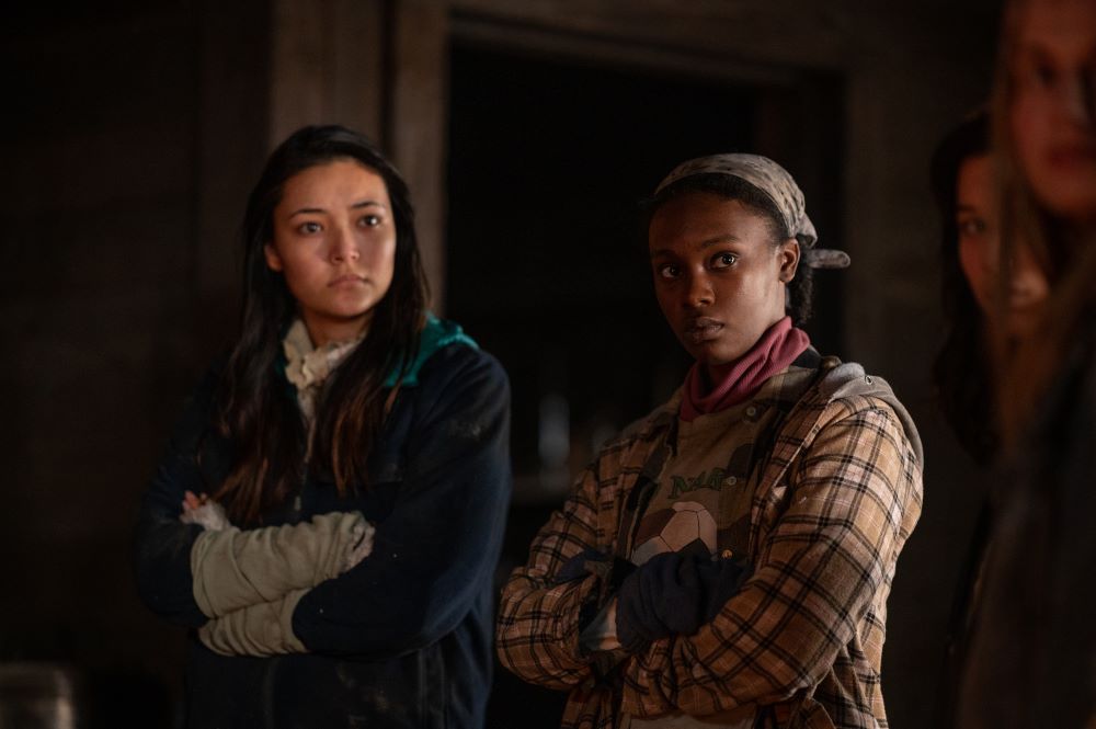 Teen Mari and teen Akilah stand next to each other in the cabin while looking focused in Yellowjackets Season 2 Episode 7, "Burial."
