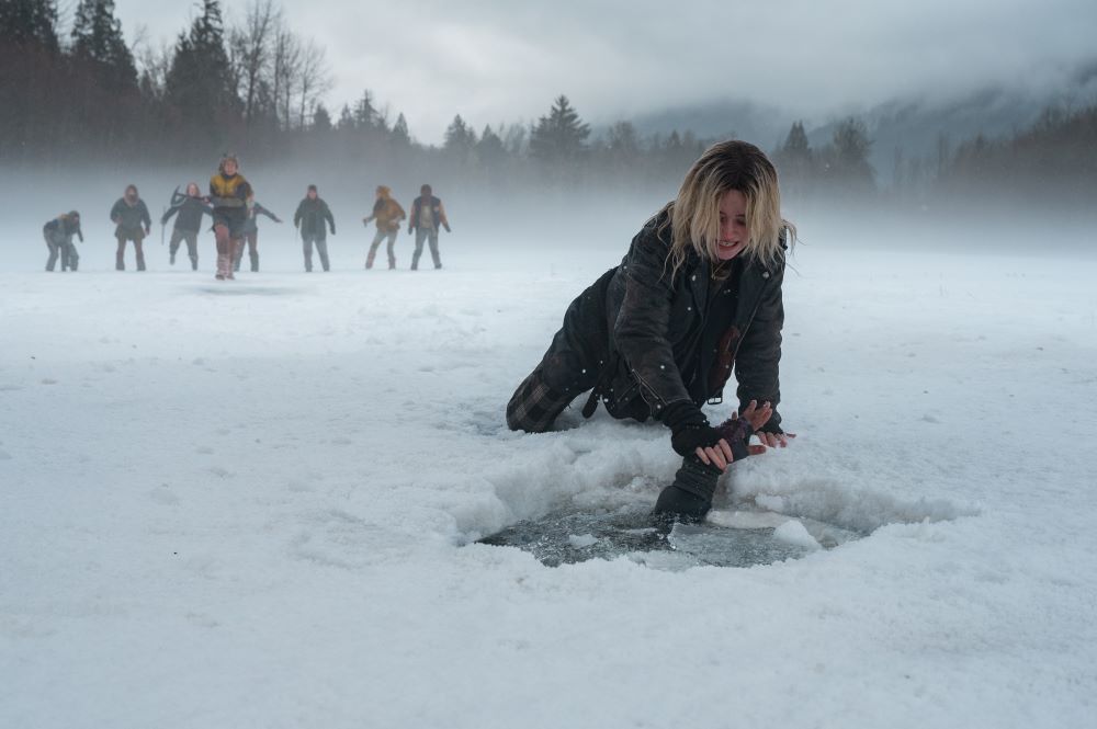 Teen Natalie reaches through a hole in an icy lake to save Javi while the other teens stand at a distance behind her in Yellowjackets Season 2 Episode 8, "It Chooses."