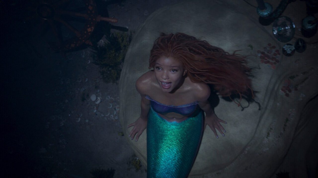 Halle Bailey as ariel looks longingly towards the surface as she sits on a rock in The Little Mermaid.