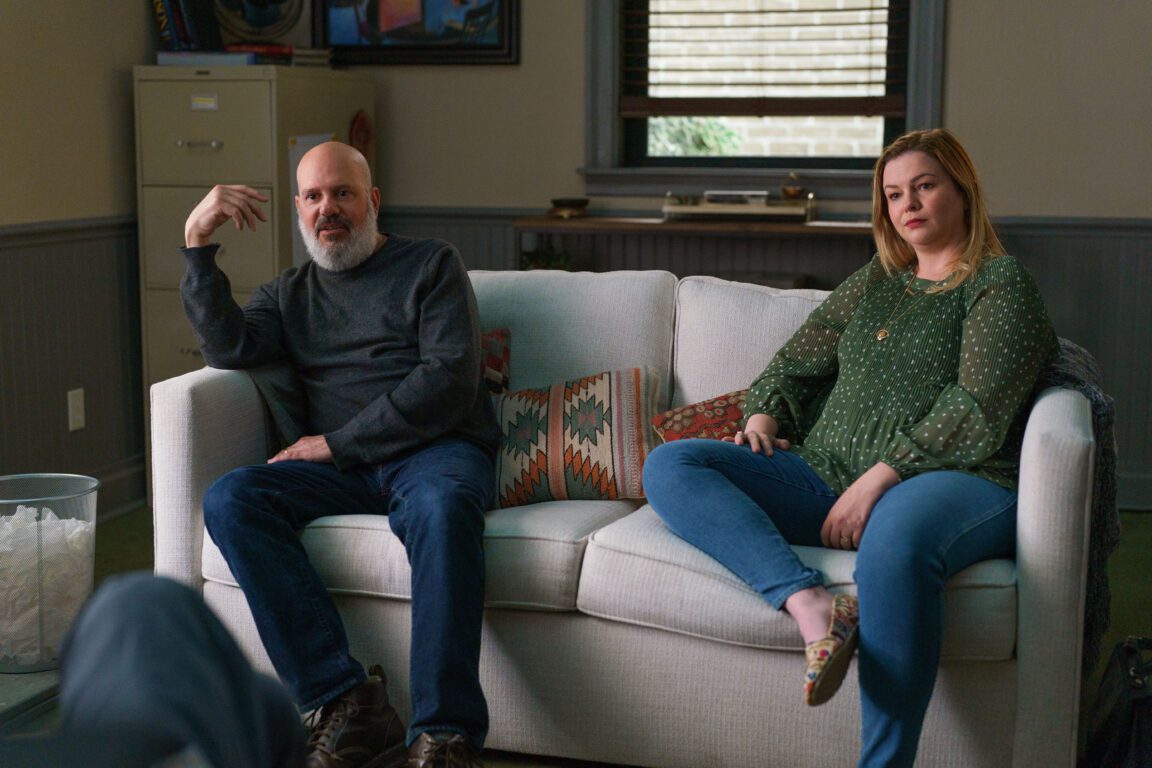 David Cross and Amber Tamblyn sit on a sofa and stare across the camera as they listen intently in You Hurt My Feelings. 