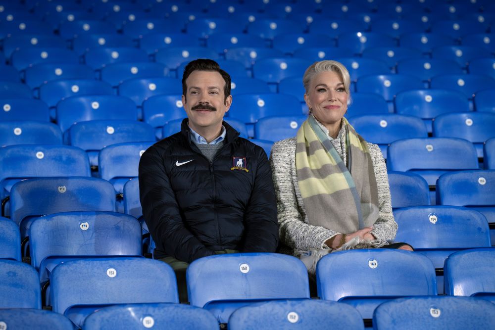 Ted and Rebecca sit in the stands at Richmond while smiling in Ted Lasso Season 3 Episode 12, "So Long, Farewell."