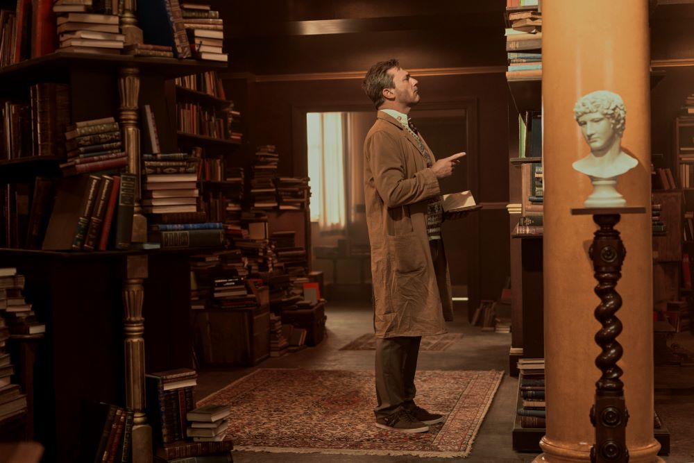 Gabriel stands in a book store while looking up at a bookshelf in Good Omens Season 2 Episode 2, "Chapter 2: The Clue."