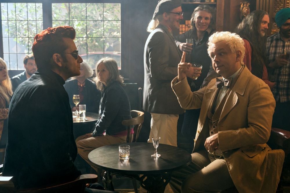 Crowley and Aziraphale sit at a small table in a crowded pub in Good Omens Season 2 Episode 2, "Chapter 2: The Clue."