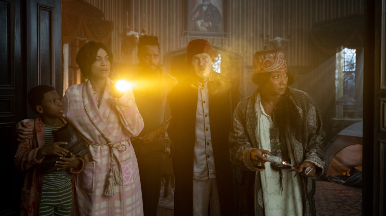 Chase Dillon, Rosario Dawson, LaKeith Stanfield, Owen Wilson and Tiffany Haddish shine flashlights as they look around a corner in Haunted Mansion. 