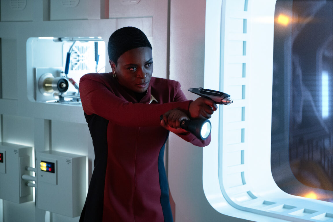 Uhura wears her red Starfleet uniform while holding a weapon and looking serious in Star Trek: Strange New Worlds Season 2 Episode 6, "Lost in Translation."