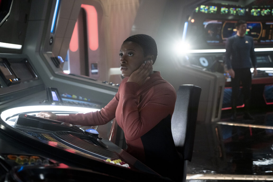 Celia Rose Gooding as Uhura in the Star Trek: Strange New Worlds season 2 finale, "Hegemony." She's serious as she works at her station on the Enterprise bridge at red alert.
