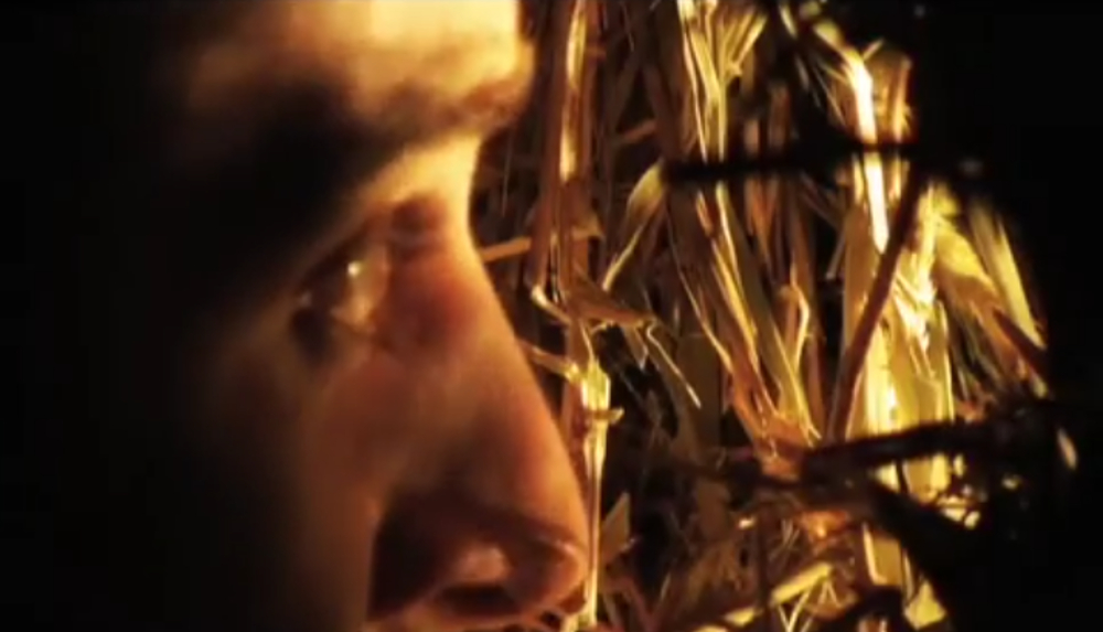 A face peers through a stack of hay in the horror movie Plasterhead.