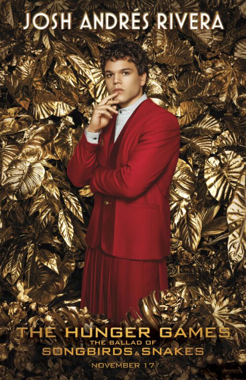 Josh Andrés Rivera as Sejanus Plinth in a red suit in front of gold leaves and flowers.