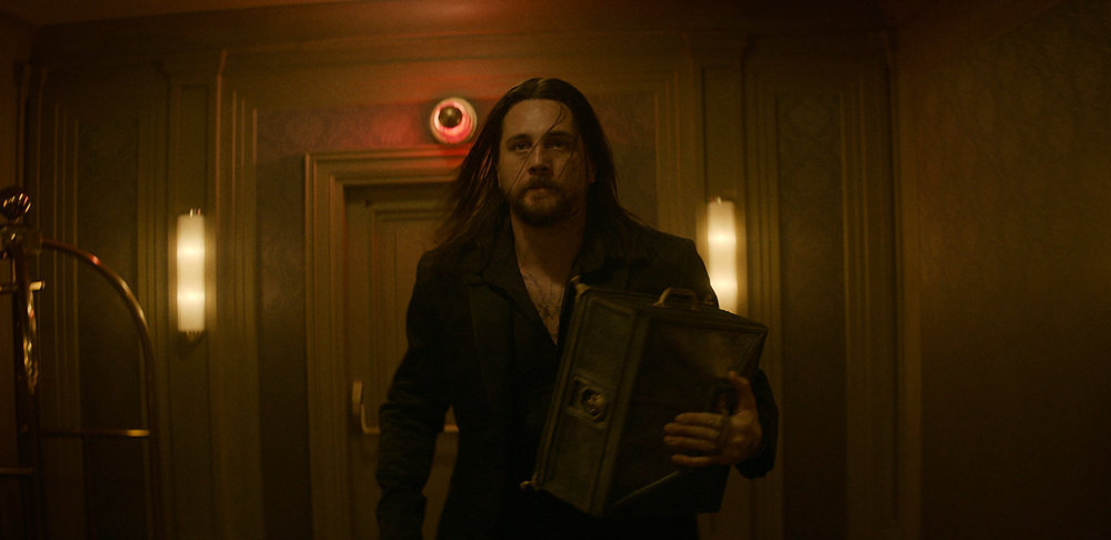 Frankie walks through a dark room while carrying an ancient coin press in The Continental: From the World of John Wick, Season 1 Episode 1, "Night 1."