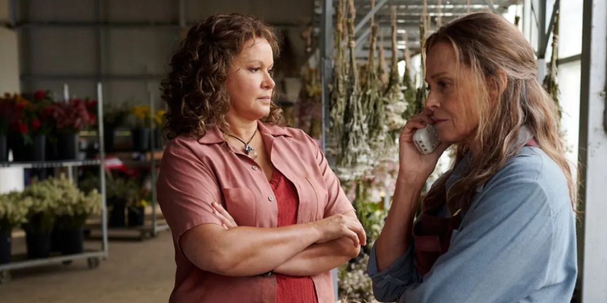 Leah Purcell in a pink shirt standing next to Sigourney Weaver talking on the phone.