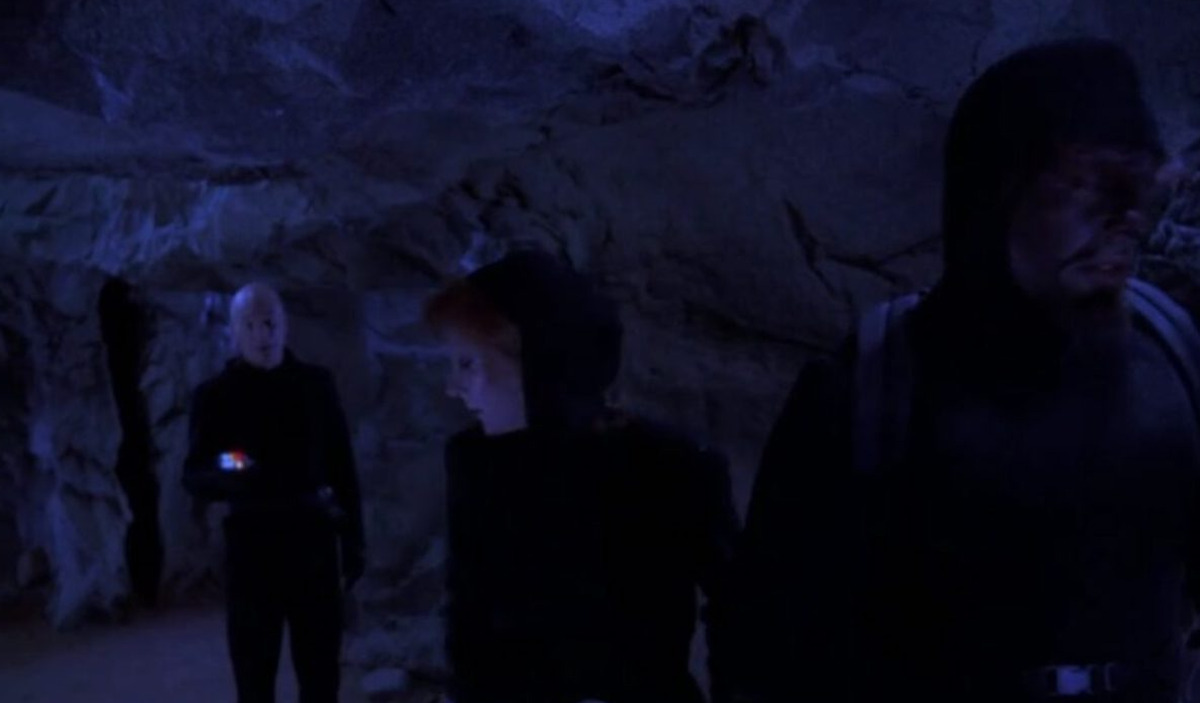 Jean-Luc Picard stands in a dark cave while talking to Beverly Crusher and Worf in Star Trek: The Next Generation. 