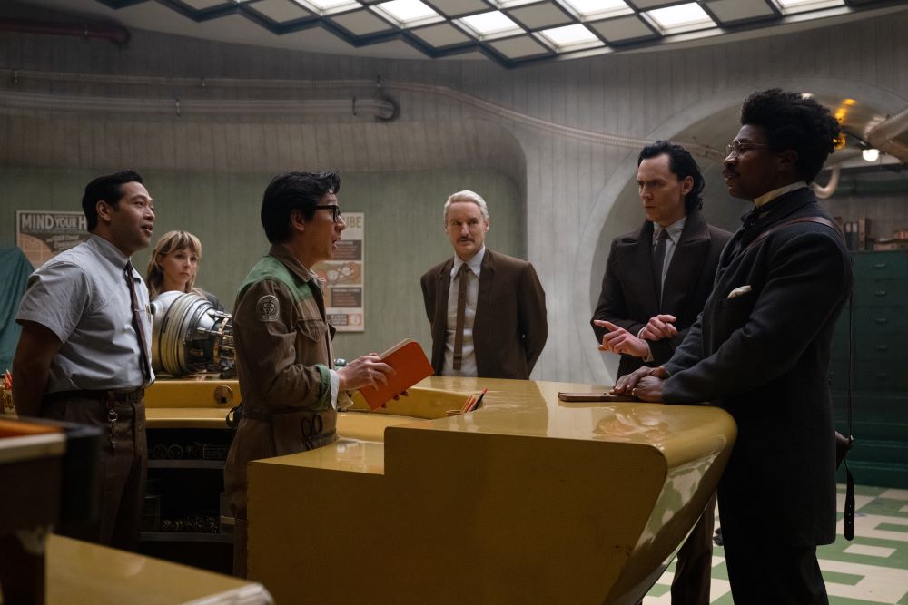 Casey, Sylvie, O.B., Mobius, Loki and Victor Timely stand in a room with an orange desk, white walls and florescent lights in Loki Season 2 Episode 4, "Heart of the TVA."
