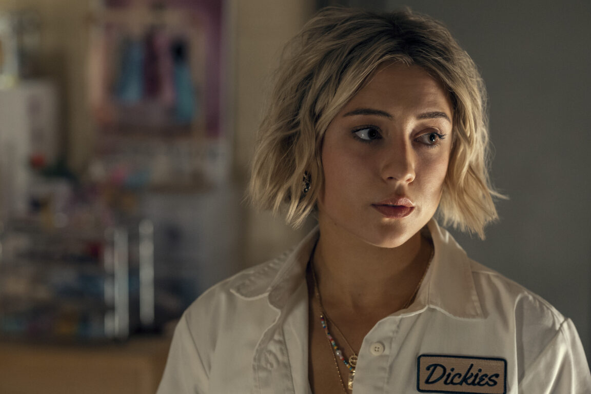 Emma Meyer stands in her college dorm room while wearing a white short-sleeved Dickies shirt with a short blonde bob while looking off-screen in Gen V Season 1 Episode 1, "God U."