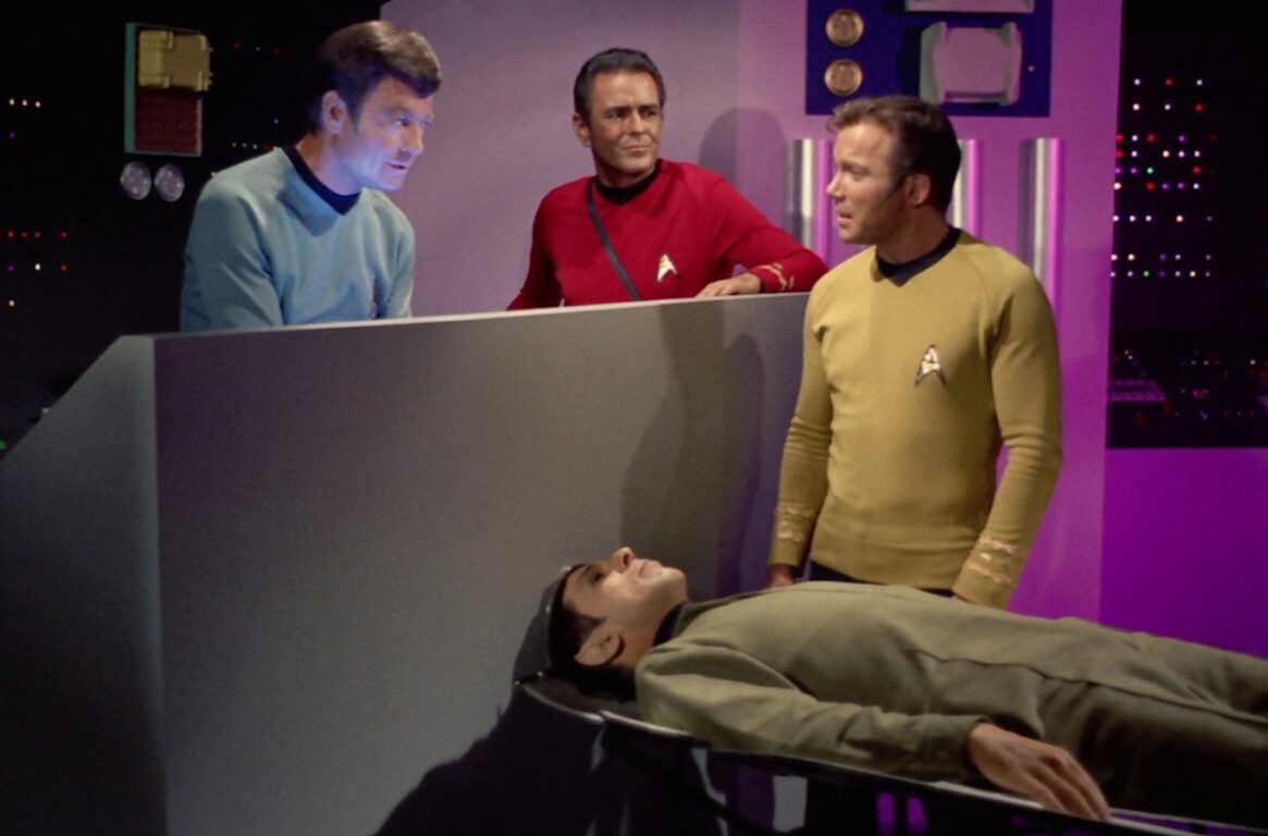 McCoy (DeForest Kelly) and Kirk (William Shatner) discuss the condition of Spock (Leonard Nimoy), who is lying unconscious.