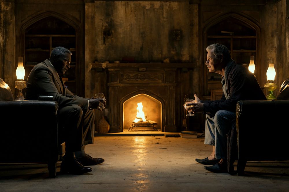 C. Auguste Dupin and Roderick Usher sit across from each other in front of a fire at night in The Fall of the House of Usher Season 1 Episode 4, "The Black Cat."