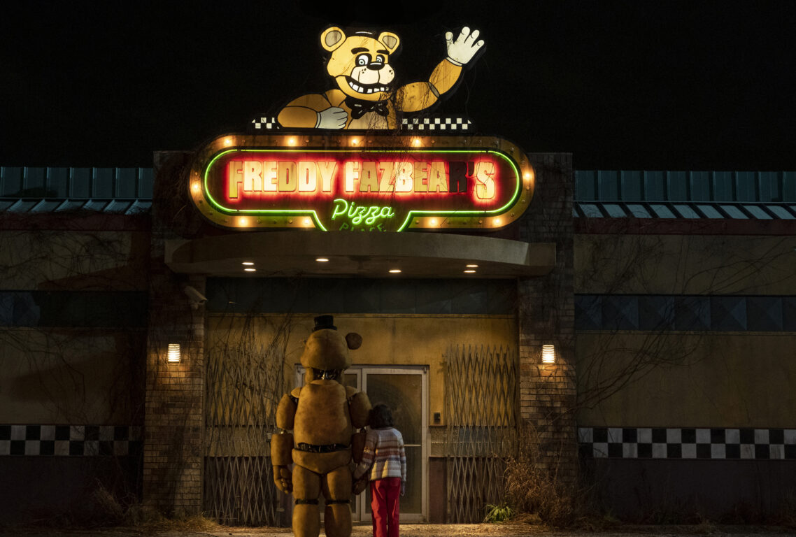 Golden Freddy (Kevin Foster) and Abby (Piper Rubio) stand in front of the pizzeria in Five Nights at Freddy's