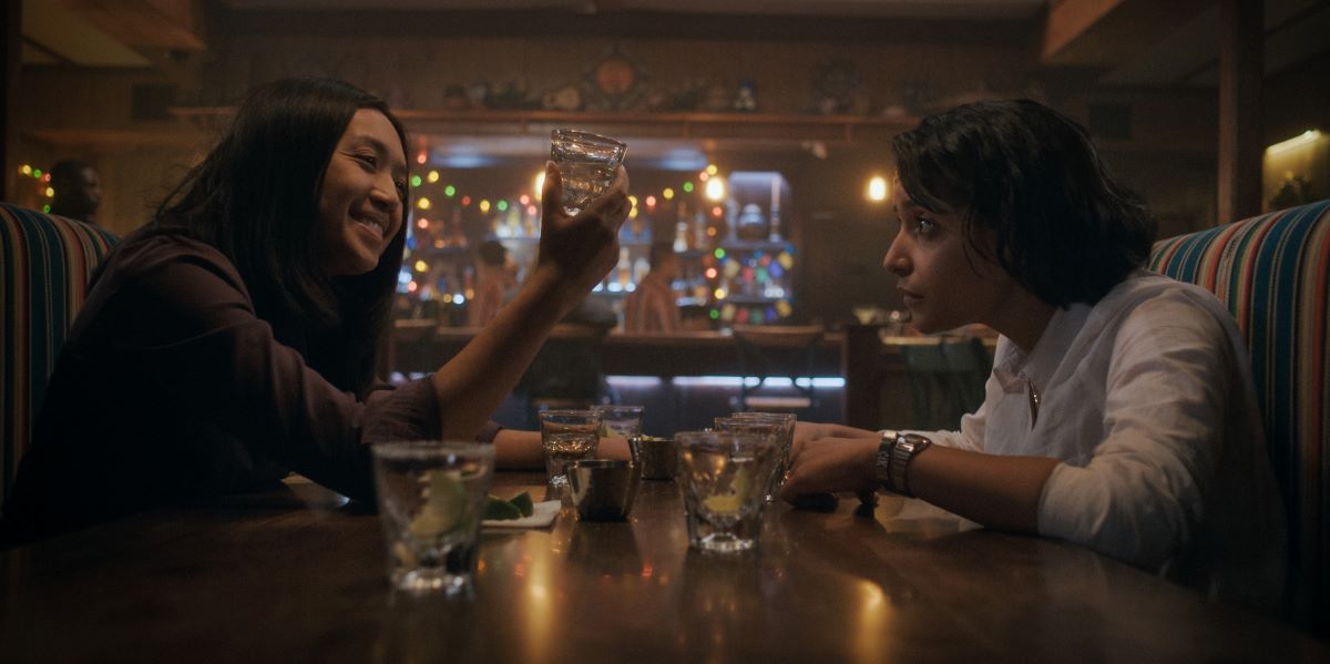 Kelly Baldwin and Aleida Rosales sit across from each other at a restaurant while drinking shots and laughing in For All Mankind Season 4 Episode 2, "Have a Nice Sol."