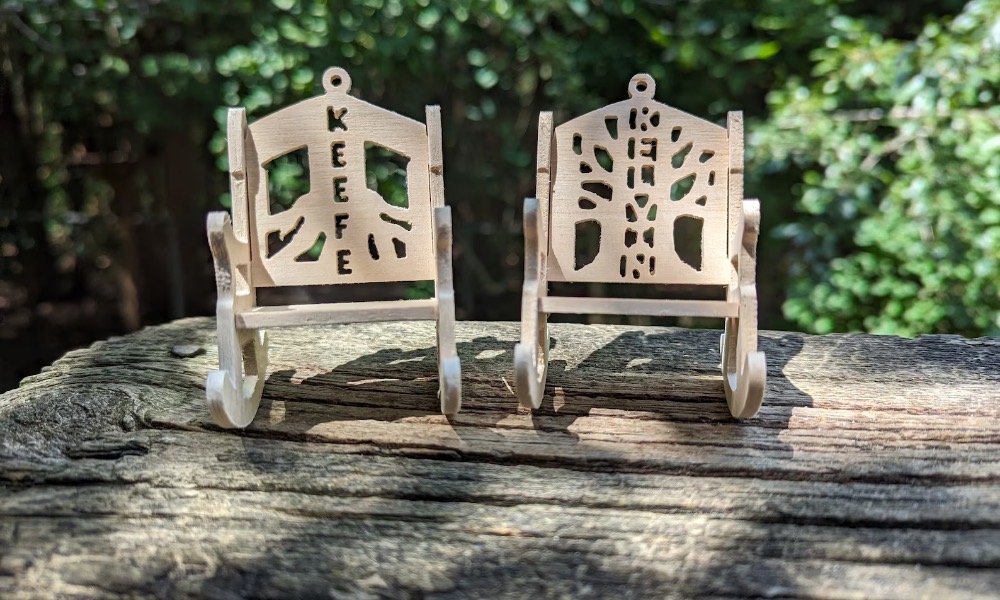 Two tree ornaments. They are rocking chairs. One has the name Keefe carved into the back, the other Kelvin 