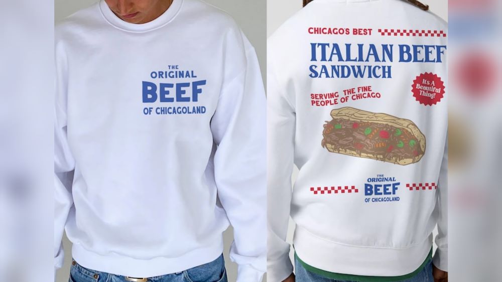 A white sweatshirt inspired by the TV series The Bear with "The Original BEEF of Chicagoland" in blue text on the front and a design of an Italian beef sandwich on the back. 
