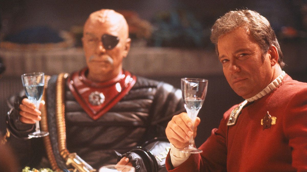 Kirk (William Shatner) raises as glass of Romulan Ale in the foreground while Chang (Christopher Plummer) does the same behind him.