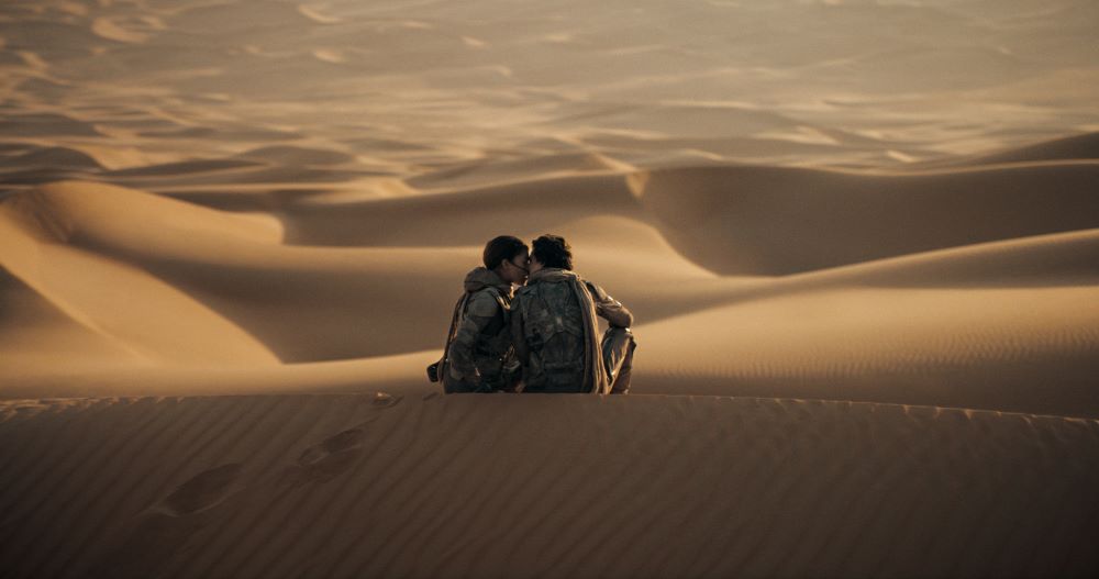 Chani and Paul Atreides cuddle while sitting in the sandy desert in Dune 2.