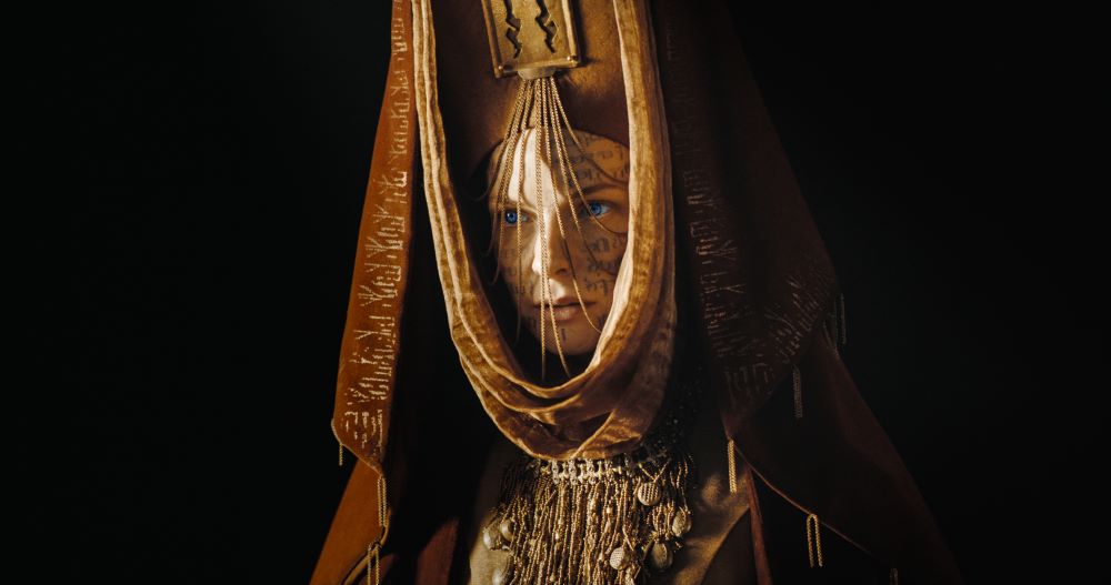 Lady Jessica wears an elaborate dark brown velvet hood with tassels while looking serious in Dune 2.
