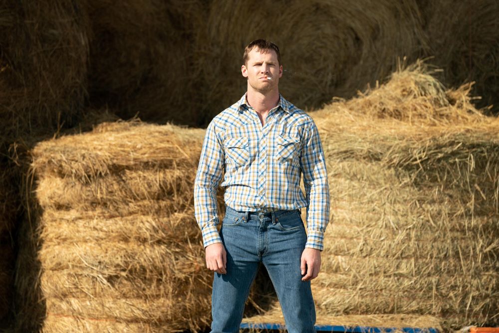 Wayne wears a plaid button-down shirt and jeans while standing next to piles of hay in Letterkenny Season 12 Episode 4, "Snooters."