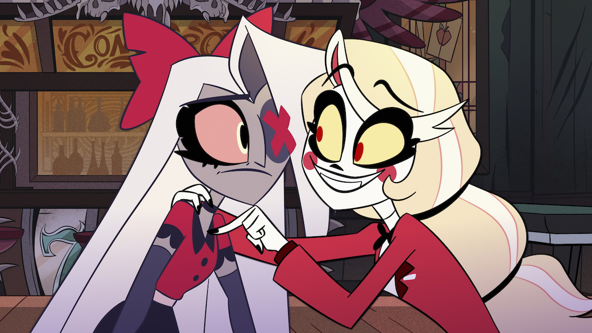 Charlie smiles while putting her arms around Vaggie's shoulders, who looks apprehensive.