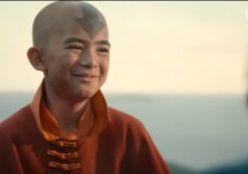 A scene from Avatar: The Last Airbender. Aang, an Asian boy with a bald head and a blue arrow tattoo, smiles at someone offscreen.