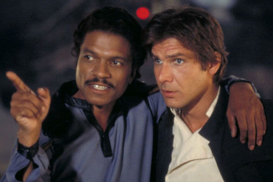lando calrissian stands with his hand round han solo's shoulders and points in a direction
