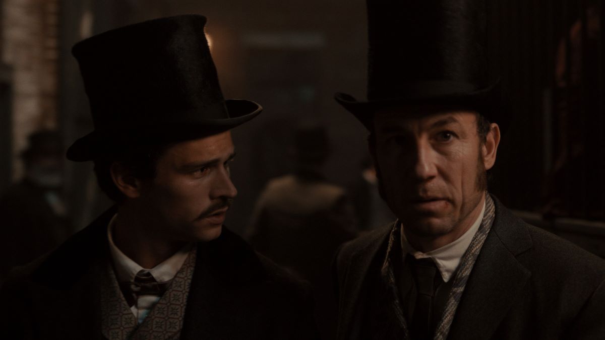 Eddie and Edwin Stanton stand together in a dimly lit alley. Both wear stovepipe top hats. Eddie is turned toward Edwin while Edwin looks ahead.