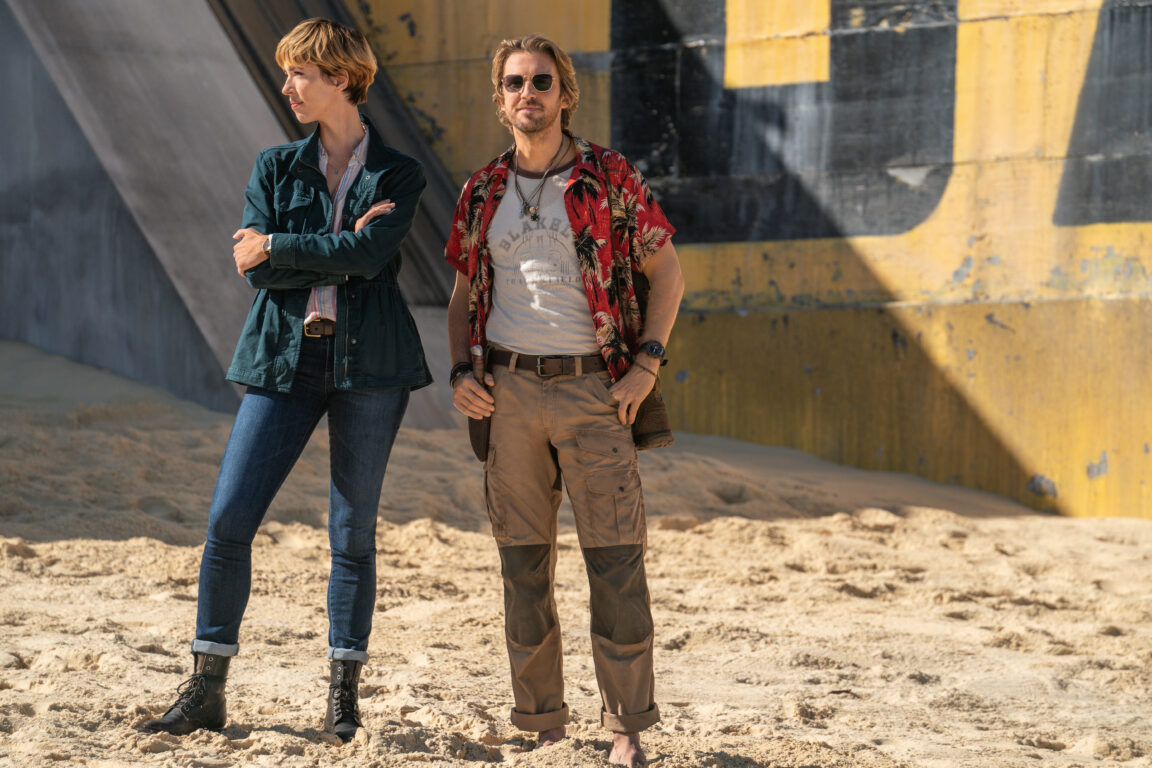 Rebecca Hall and Dan Stevens stand in a desert environment as they watch something happen off-screen in Godzilla x Kong: The New Empire