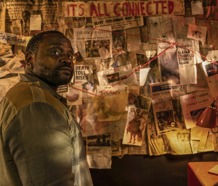 Brian Tyree Henry looks at the camera as he stands in front of his conspiracy theory board in Godzilla x Kong: The New Empire