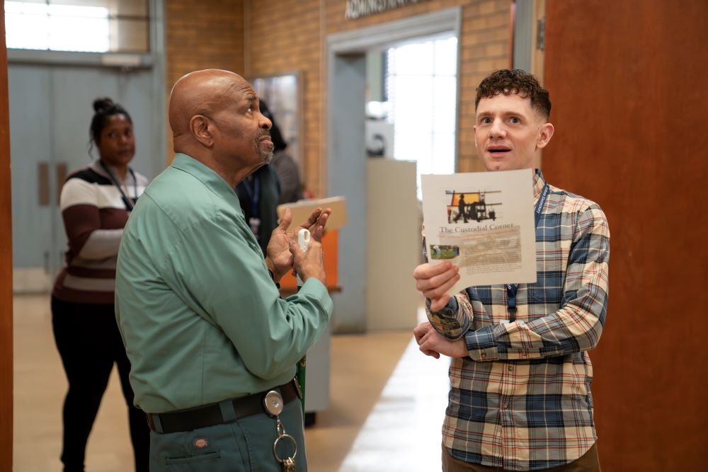 Mr. Johnson talks to Jacob in a school hallway, who holds a newsletter in his hand, on Abbott Elementary Season 3 Episode 9, "Alex."