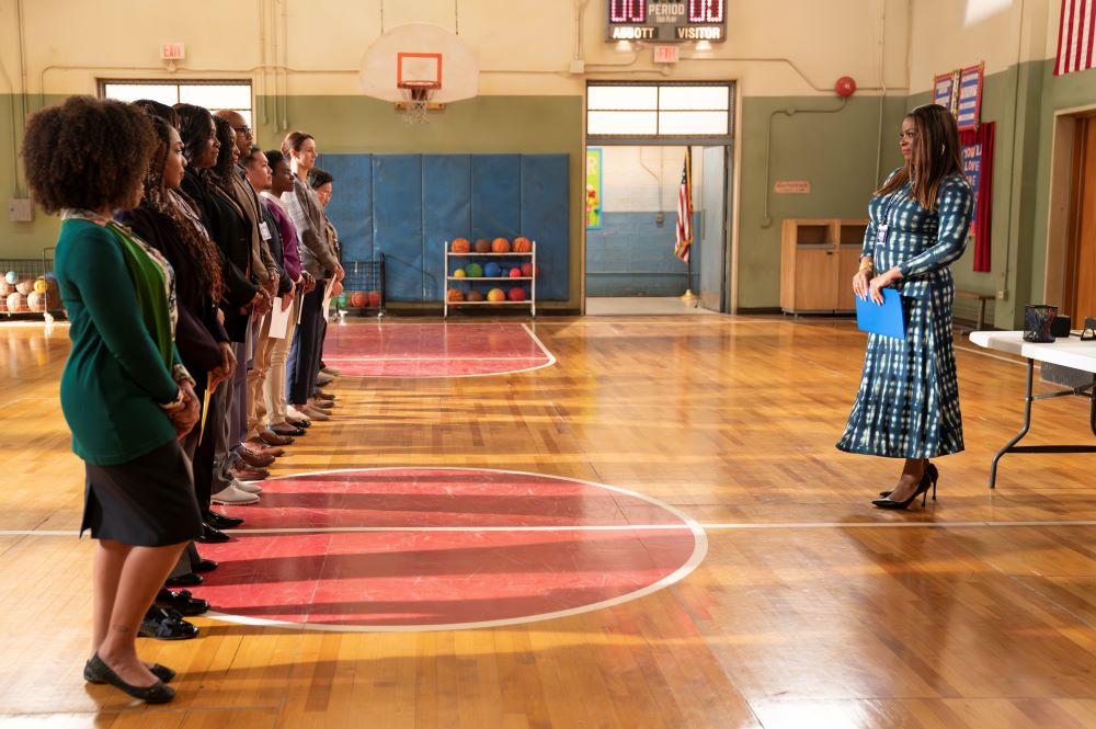 Ava Coleman stands in a school gymnasium while a row of potential teaching candidates stand in a line across from her on Abbott Elementary Season 3 Episode 9, "Alex."