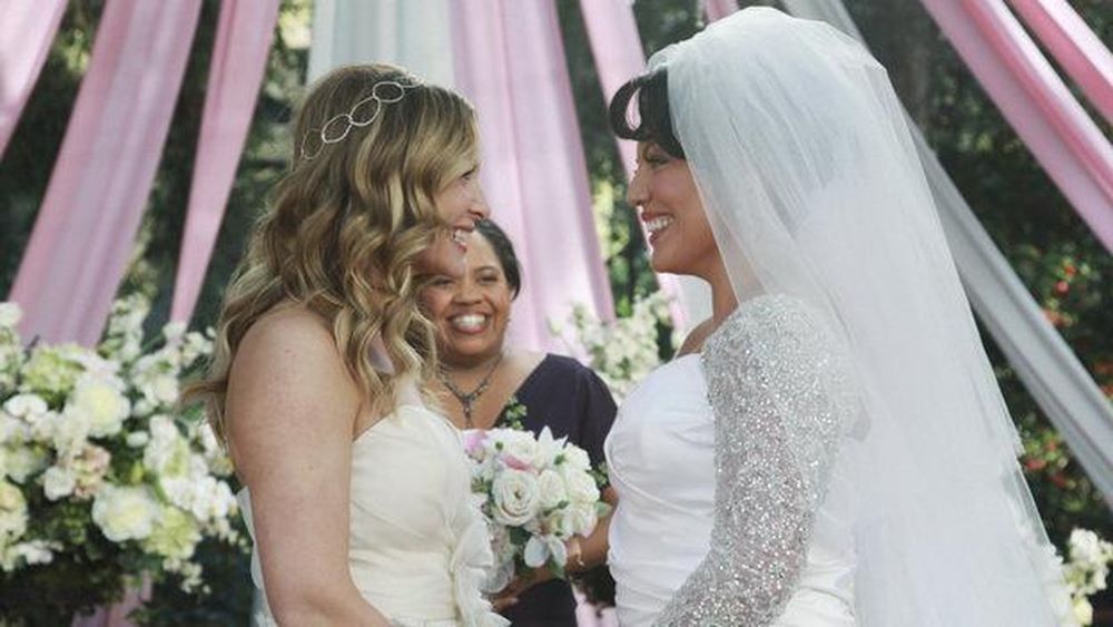 Arizona and Callie wear wedding dresses while smiling and standing at an altar on Grey's Anatomy. 