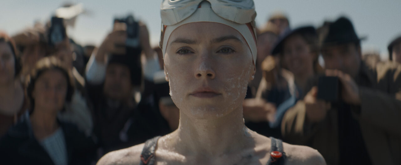 Daisy Ridley stares at the camera in concentration. She wears a swim cap and goggles in the movie Young Woman and the Sea.