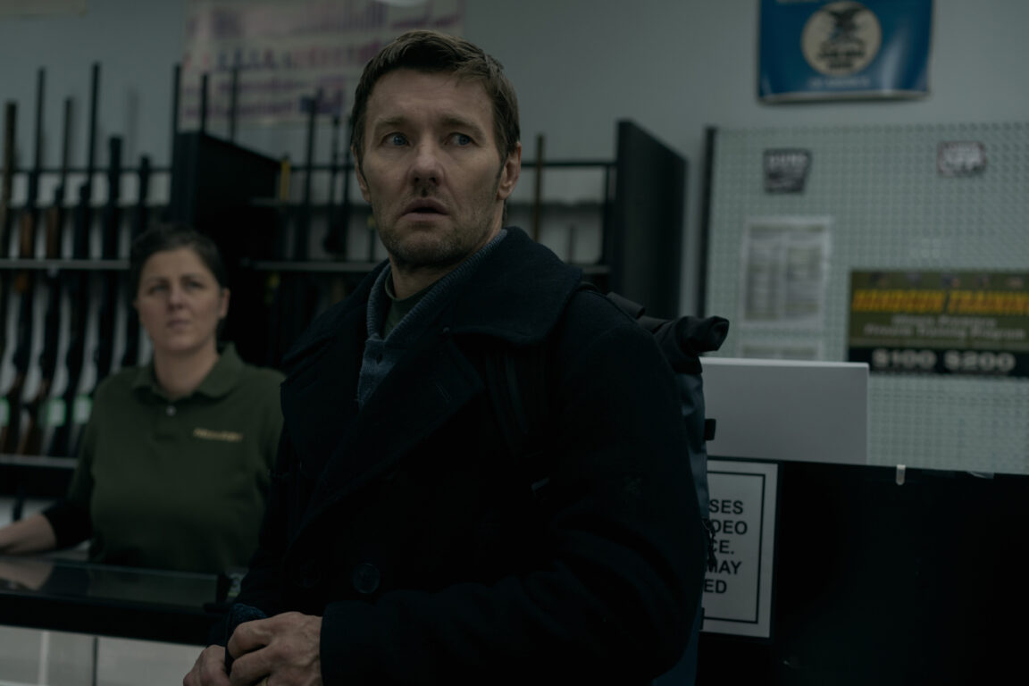 Jason looks straight ahead while standing in a weapons store. 