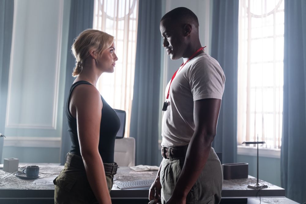 Ruby Sunday and The Doctor wear military garb while standing in a room suffused with natural light.