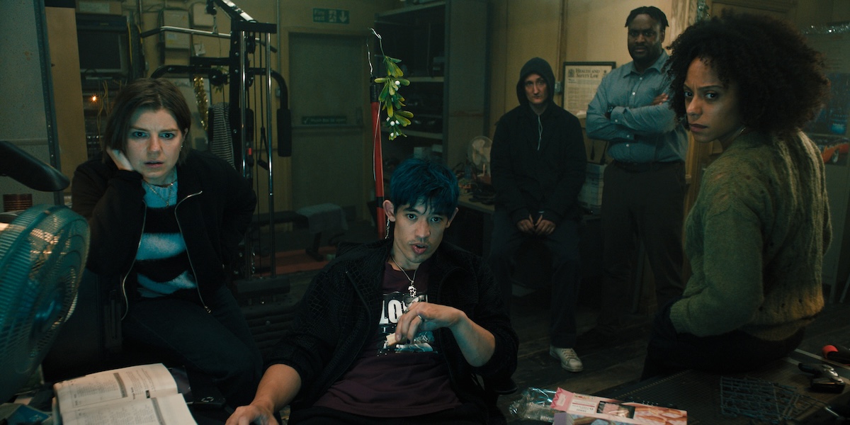 5 members of Slough House crowd around a desk and look at a computer in season 4 of apple tv+'s slow horses
