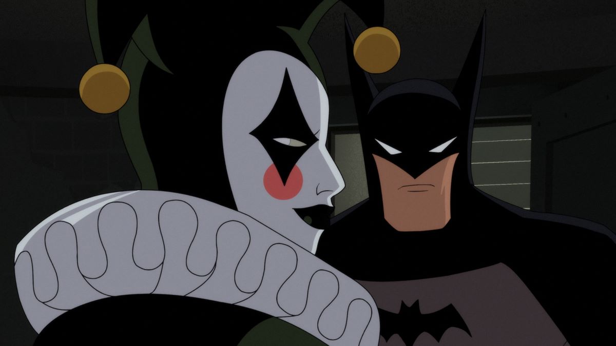 Harley Quinn looks to the right in profile with Batman approaching. She's dressed in her jester's costume with painted face make-up and wide white ruffled collar. He wears the black bat cowl mask over a grey skin suit. Batman: Caped Crusader Season 1 Episode 5