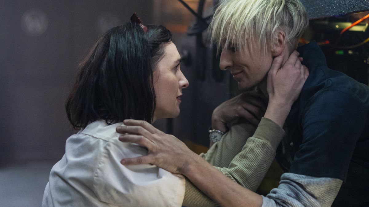 Audrey and Bess hold each other, facing in profile. Audrey, on the left, wears a white, short-sleeved blouse over an olive green thermal shirt and her hair is tied back with a band. Bess's hair is rumpled. She has on a dark blue short sleeved shirt over grey thermals on Snowpiercer Season 4 Episode 2, "The Sting of Survival."
