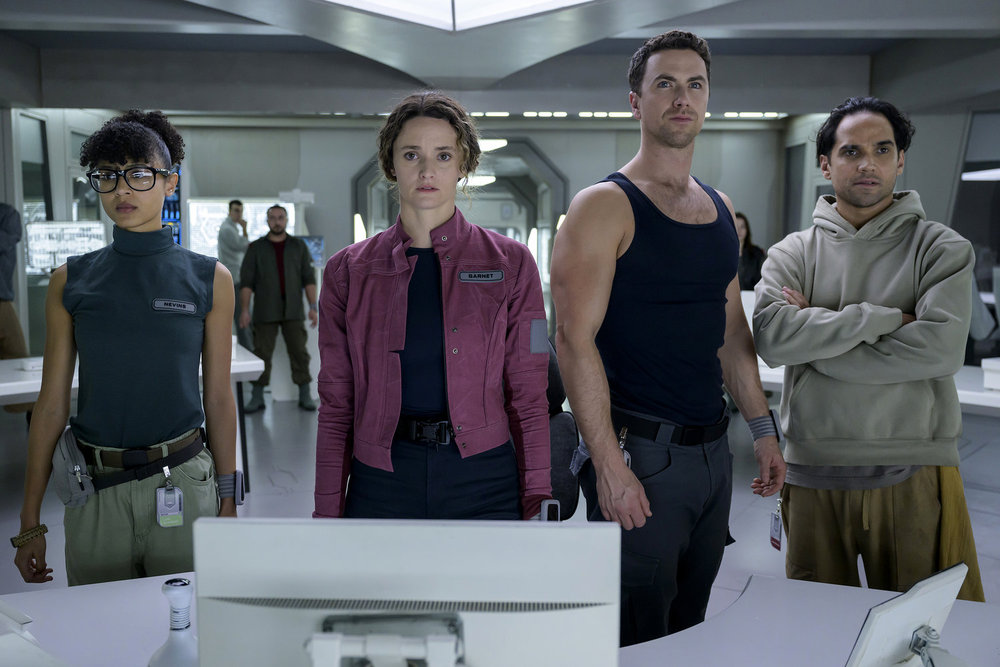 Alicia, Capt. Garnet, Lt. Brice and Ian stand on the bridge of their spaceship while looking at something off-screen on The Ark Season 2 Episode 12, "Fortunate."