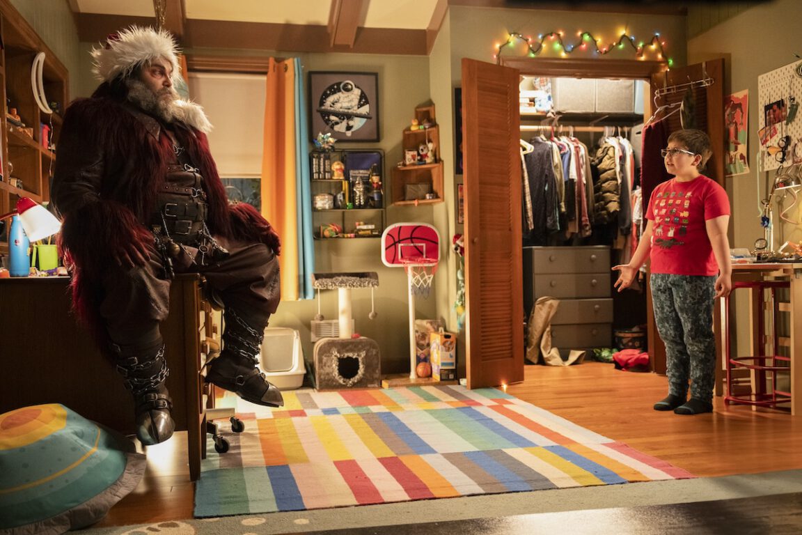 a bearded Santa looking man (Jack Black) talks to a boy wearing a red shirt in his bedroom. From Dear Santa on Paramount plus