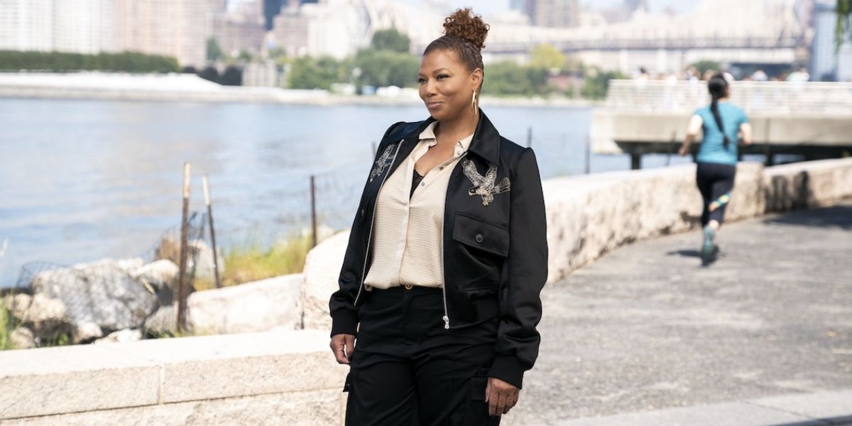 Queen Latifah smiling while standing on the street near a river on The Equalizer.
